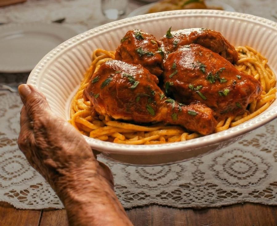 Manos de la abuela sirviendo una fuente de tallarines rojos con pollo